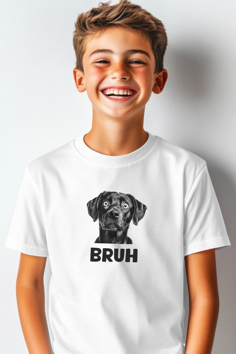 A smiling young boy wearing a white T-shirt featuring a black-and-white dog illustration and the word “BRUH” in bold lettering.