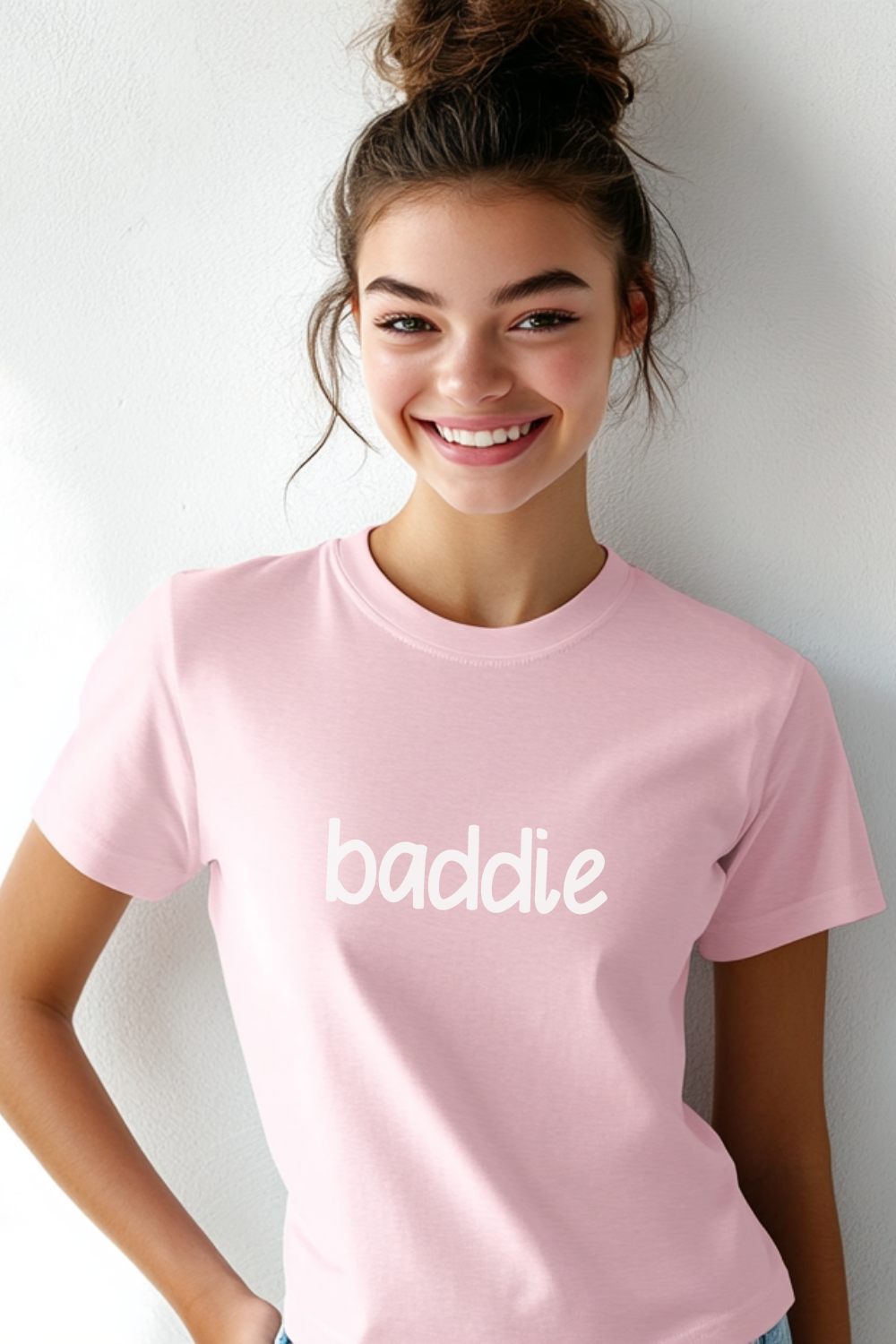 A smiling young woman wearing a pink T-shirt with “baddie” in white lettering, showcasing a trendy and confident streetwear look.