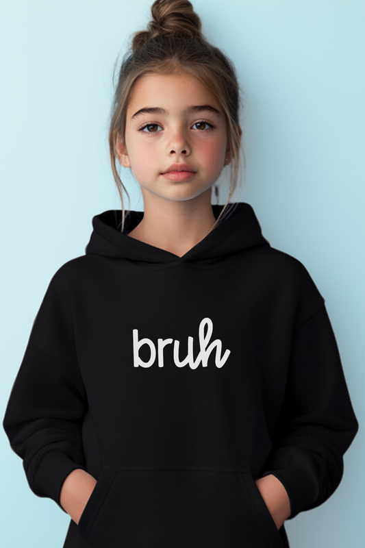 A girl wearing a sleek black unisex youth hoodie featuring a stylish cursive design that spells out "bruh." This edgy streetwear piece offers modern comfort and trendy style, perfect for fashion-forward girls seeking urban-inspired apparel.