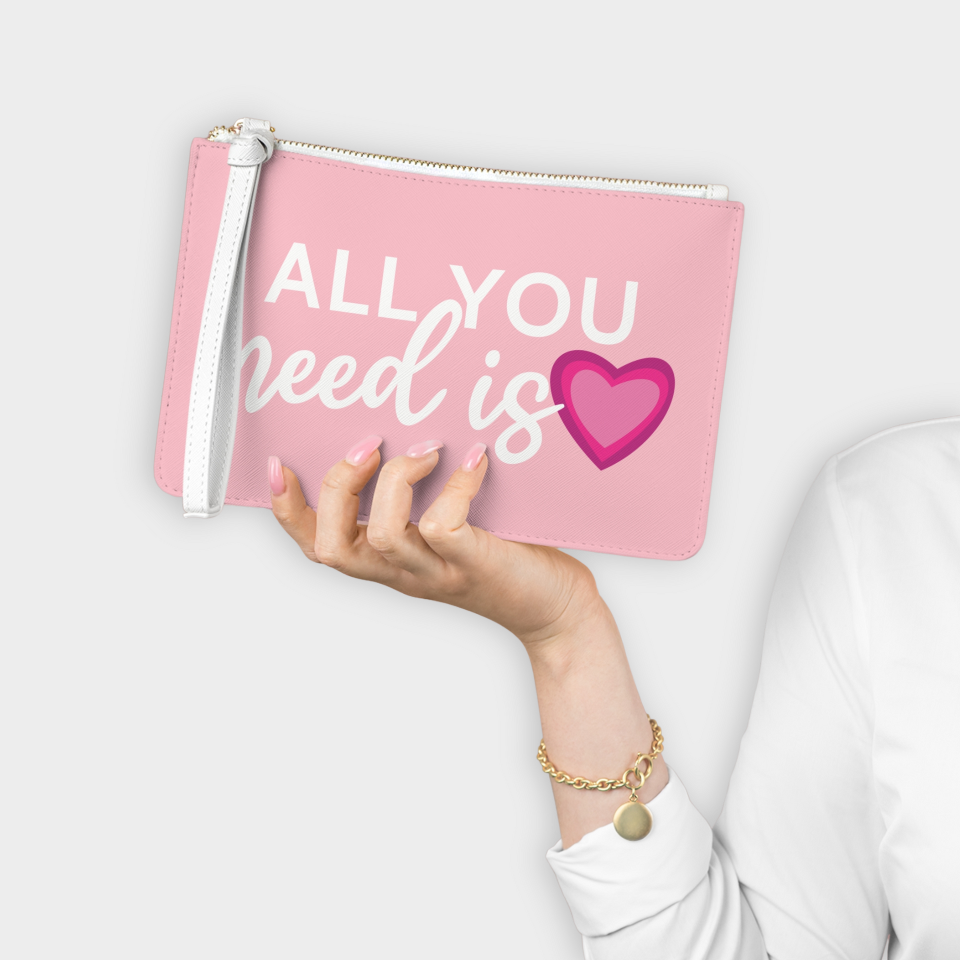 Light pink vegan leather clutch bag with 'All You Need Is Love' design featuring a cute 3-layer heart, perfect for Valentine's Day gifts or year-round use. Features saffiano pattern finish, wrist strap, and two compartments for stylish and practical everyday use.