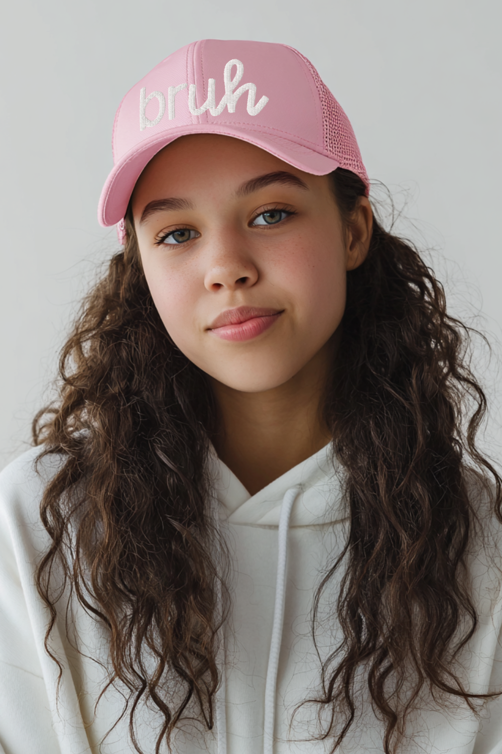 A tween girl wearing a light pink embroidered “bruh” trucker hat paired with a white hoodie. The photo showcases the hat’s mesh back, curved brim, and textured white embroidery, ideal for product listings targeting tweens and teens.